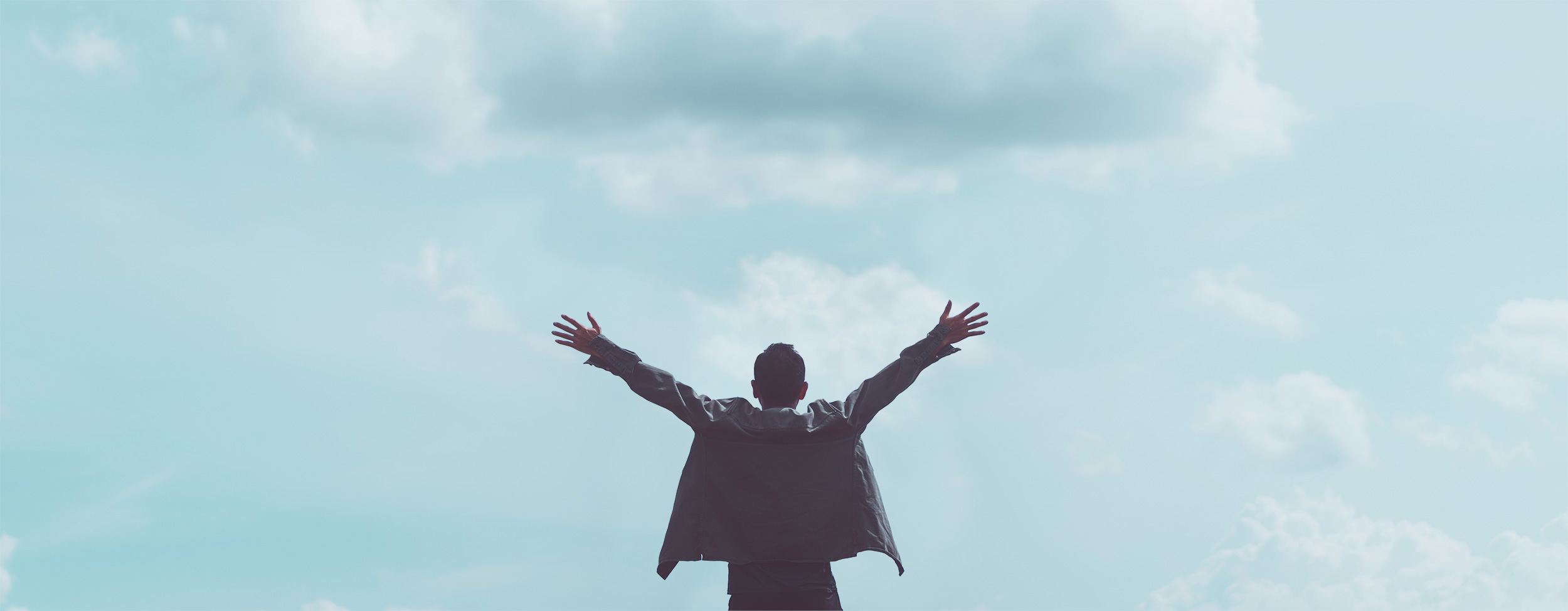 Une personne se tient debout, les bras tendus, face à un ciel nuageux, vu de dos. Le dégradé bleu-vert évoque le calme, comme si elle embrassait la liberté après une voiture tonneau, créant une atmosphère exaltante.